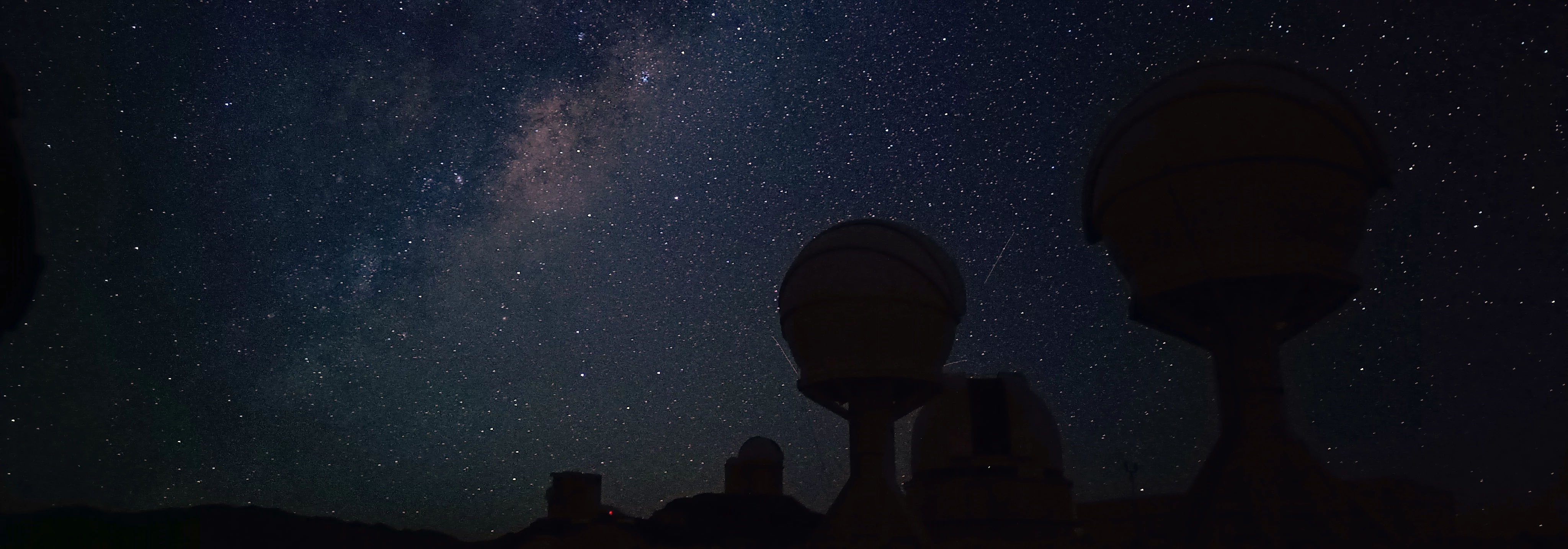 Night sky image featuring the Milky Way and telescopes at La Silla observatory.