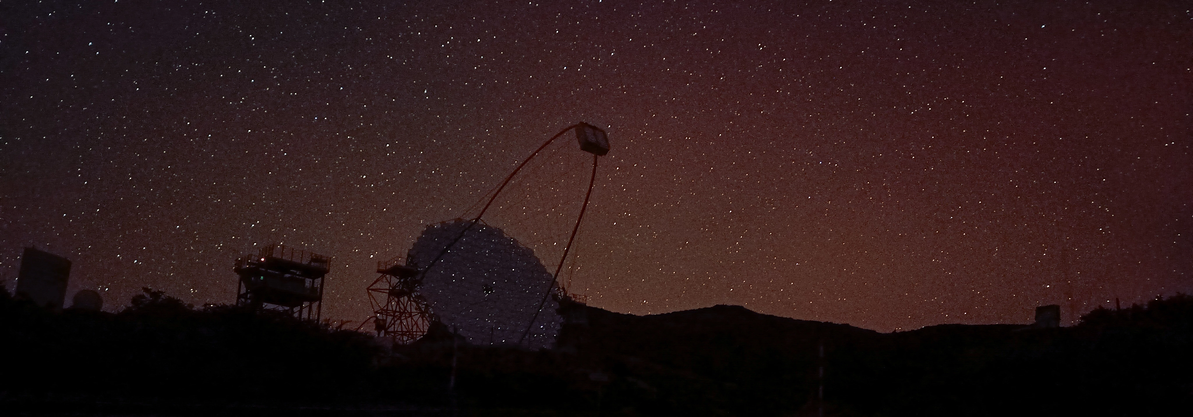 A nighttime picture of the Cherenkov Telescope Array featuring the Large Size and MAGIC groups of telescopes on La Palma. The telescope mirror reflects the starry night sky. 