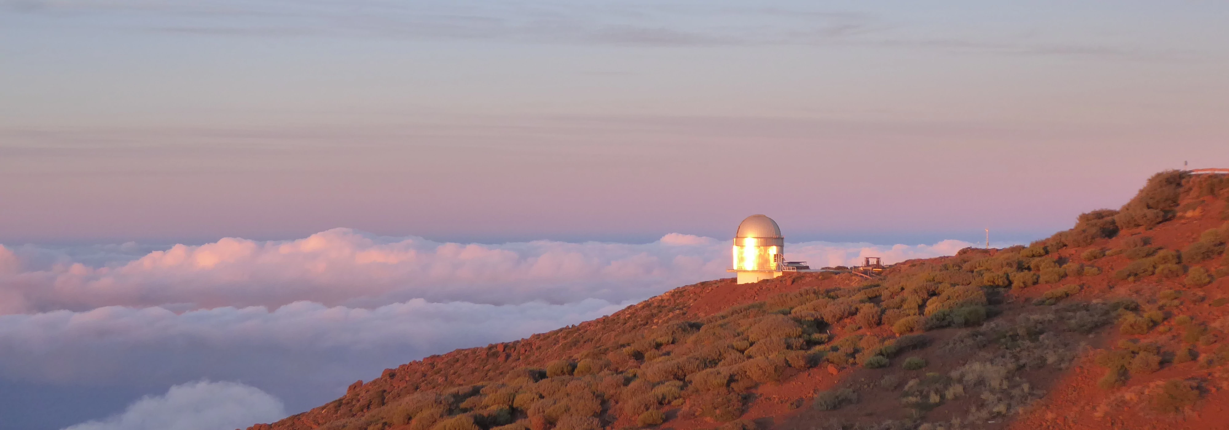 View towards the Nordic Optical Telescope during sunset, the sun has painted the mountain with a red hue.