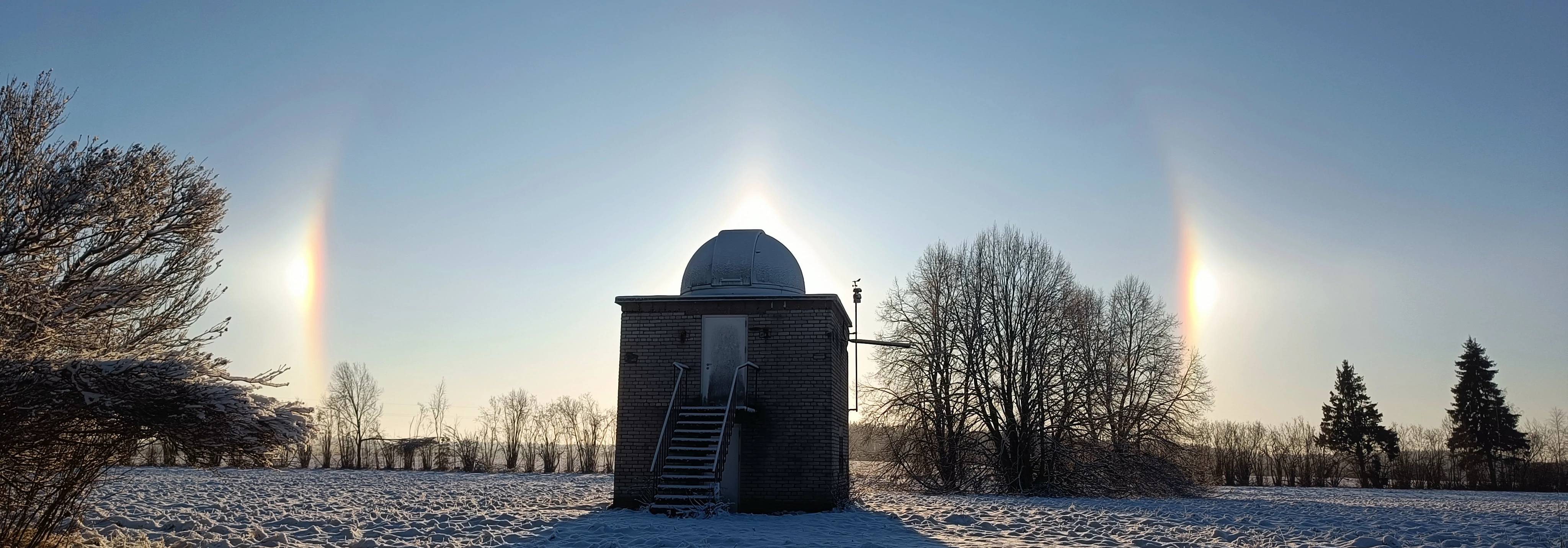 Daytime picture of the sun behind the telescope. It is a cold winter day and the sun's halo is visible surrounding the telescope dome.